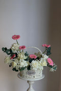 Decorative flower arrangement in a wicker basket on a white pedestal against a plain background