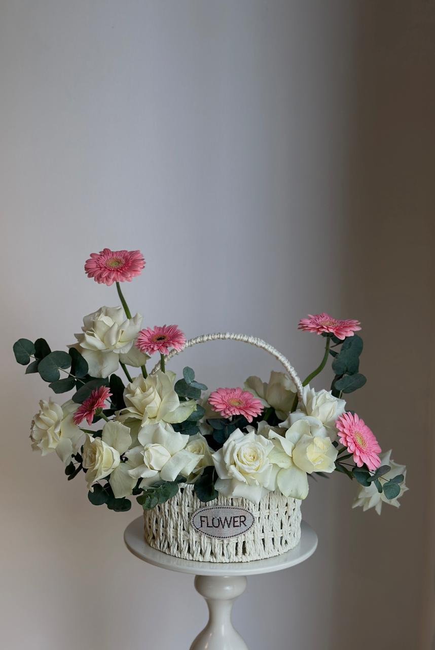 Decorative flower arrangement in a wicker basket on a white pedestal against a plain background
