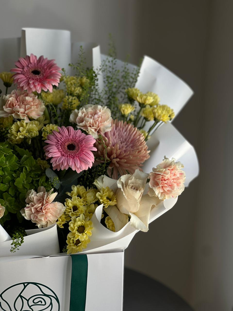 Bouquet of flowers wrapped in white paper with a green ribbon on a blurred background